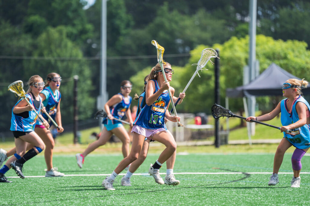 Girls wearing blue and orange lacrosse jerseys supplied by Signature during an intense game of lacrosse