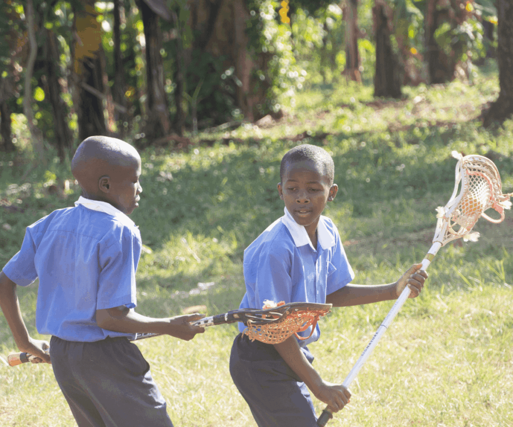 Young kids in school uniforms playing lacrosse in Uganda
